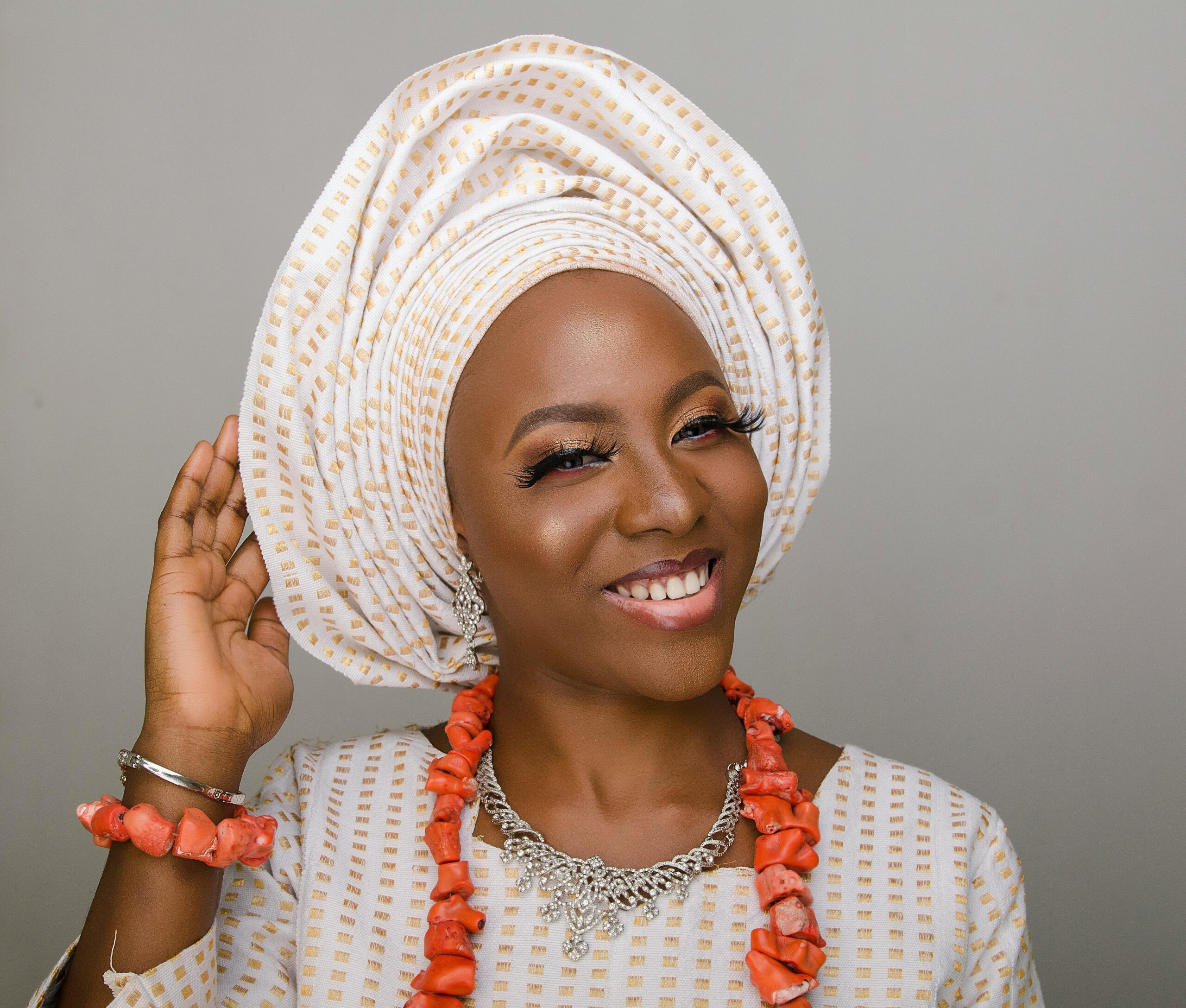 Elegant woman wearing traditional Nigerian headwrap and jewelry, smiling warmly.